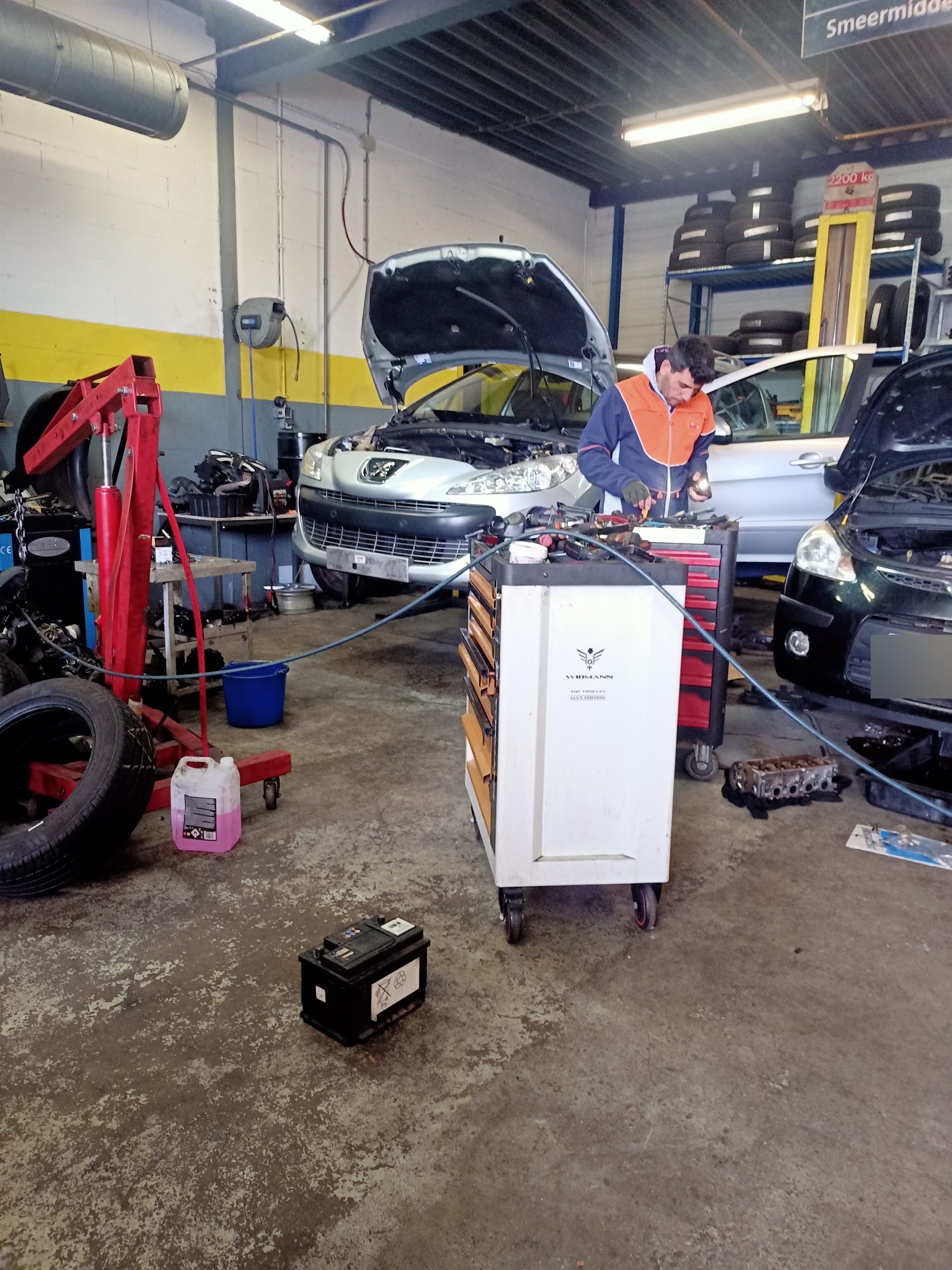 In de werkplaats van Autogarage Ster: een monteur bij de gereedschapswagen, een auto met de motorkap open en banden in het rek